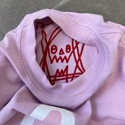 Asspizza 2025 Pink Star Tee is a dark pink T-shirt featuring a large light pink star graphic on the front. The star has a white outline and a white Happy Asspizza face design in the center. The shirt includes a red scribbled 2025 neck tag.
