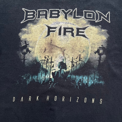 Babylon Fire 2012 “Dark Horizons” Tee is a washed black T-shirt made on a Gildan blank. The front features the album artwork for Dark Horizons, depicting a graveyard scene with a moon and clock. “Babylon Fire” text is printed at the top of the graphic, with “Dark Horizons” text below. Babylon Fire was an alternative rock band active until 2019.