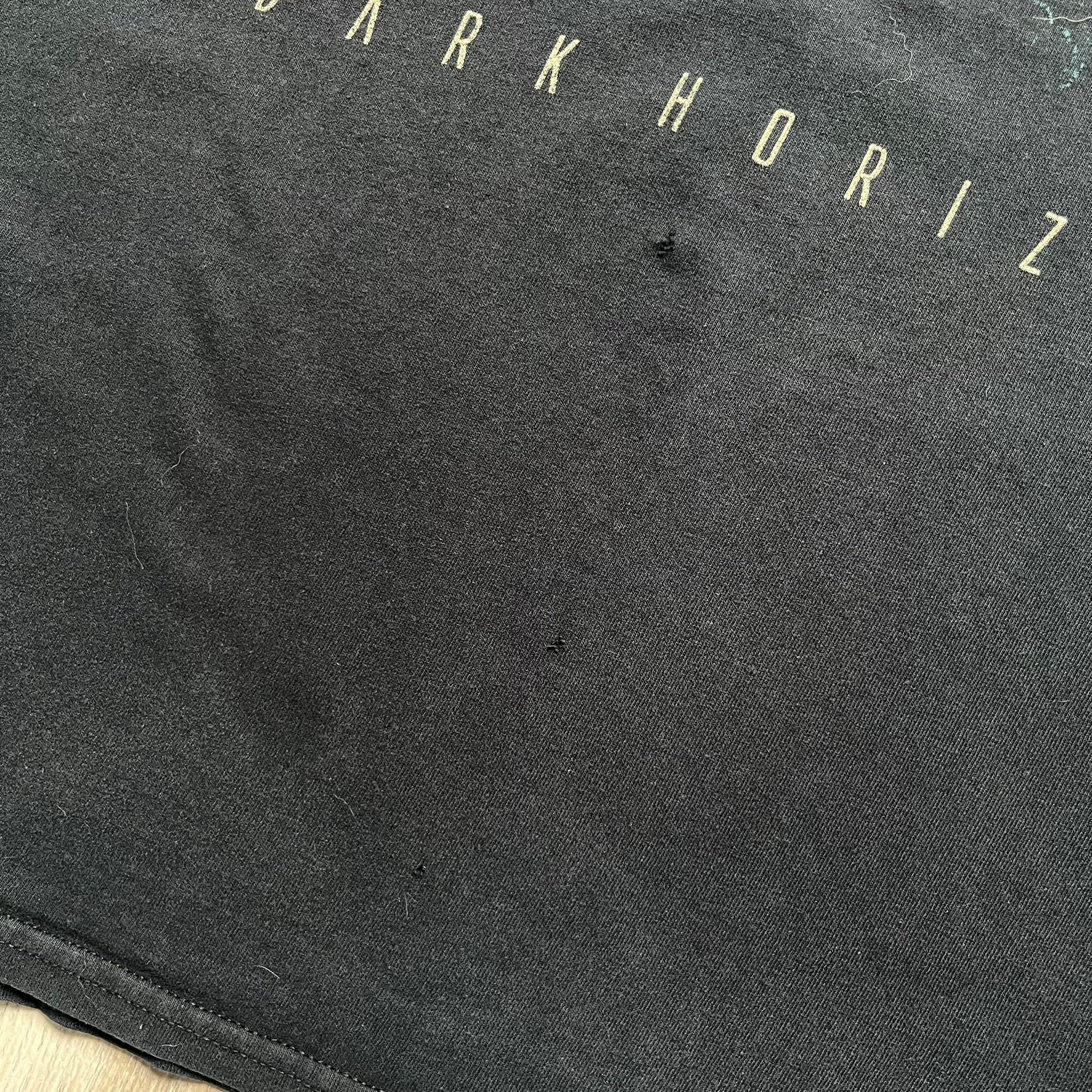 Babylon Fire 2012 “Dark Horizons” Tee is a washed black T-shirt made on a Gildan blank. The front features the album artwork for Dark Horizons, depicting a graveyard scene with a moon and clock. “Babylon Fire” text is printed at the top of the graphic, with “Dark Horizons” text below. Babylon Fire was an alternative rock band active until 2019.