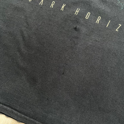 Babylon Fire 2012 “Dark Horizons” Tee is a washed black T-shirt made on a Gildan blank. The front features the album artwork for Dark Horizons, depicting a graveyard scene with a moon and clock. “Babylon Fire” text is printed at the top of the graphic, with “Dark Horizons” text below. Babylon Fire was an alternative rock band active until 2019.