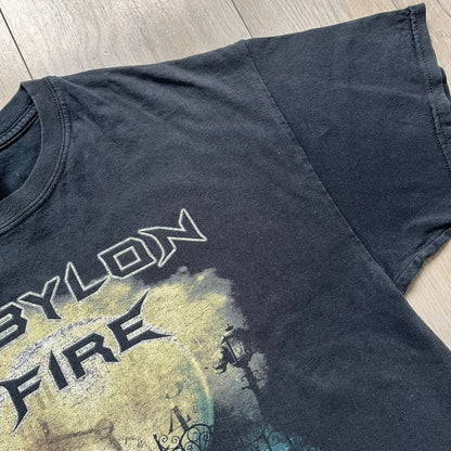 Babylon Fire 2012 “Dark Horizons” Tee is a washed black T-shirt made on a Gildan blank. The front features the album artwork for Dark Horizons, depicting a graveyard scene with a moon and clock. “Babylon Fire” text is printed at the top of the graphic, with “Dark Horizons” text below. Babylon Fire was an alternative rock band active until 2019.