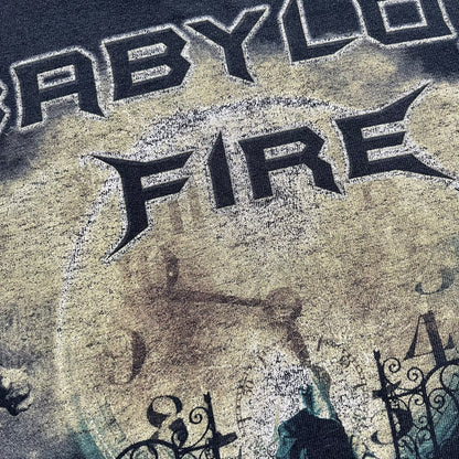 Babylon Fire 2012 “Dark Horizons” Tee is a washed black T-shirt made on a Gildan blank. The front features the album artwork for Dark Horizons, depicting a graveyard scene with a moon and clock. “Babylon Fire” text is printed at the top of the graphic, with “Dark Horizons” text below. Babylon Fire was an alternative rock band active until 2019.