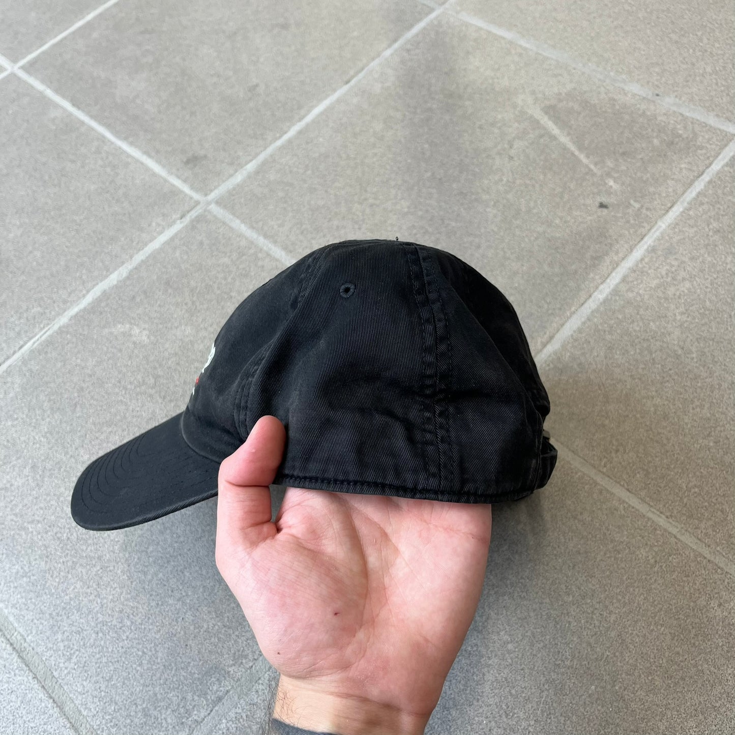 Balenciaga 2017 Political Campaign Baseball Cap features a washed black/smoked grey cotton drill construction with a curved brim. The front has an embroidered white Balenciaga logo above red and white curved stripes, with “2017” embroidered in white underneath. Made from 100% cotton.
