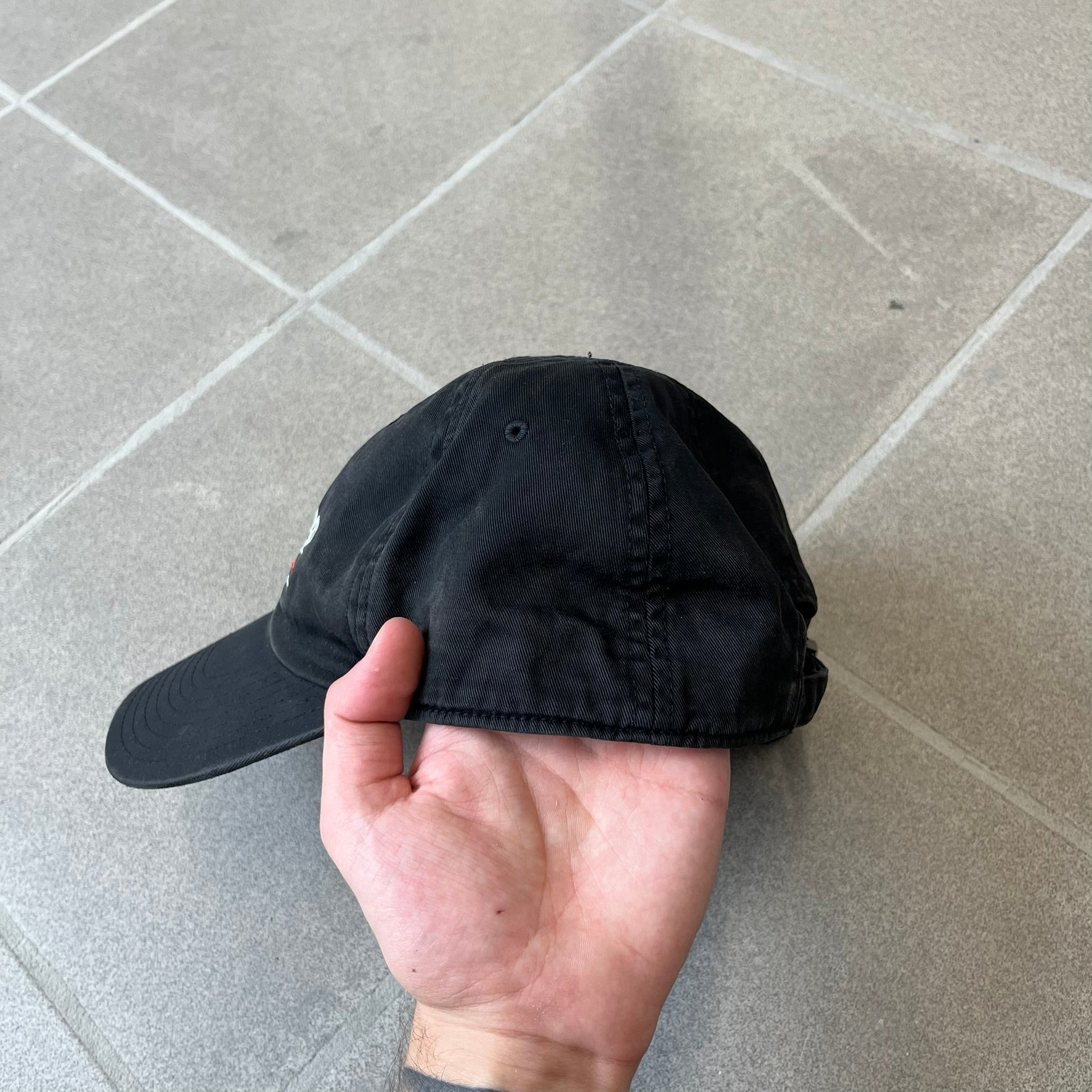 Balenciaga 2017 Political Campaign Baseball Cap features a washed black/smoked grey cotton drill construction with a curved brim. The front has an embroidered white Balenciaga logo above red and white curved stripes, with “2017” embroidered in white underneath. Made from 100% cotton.
