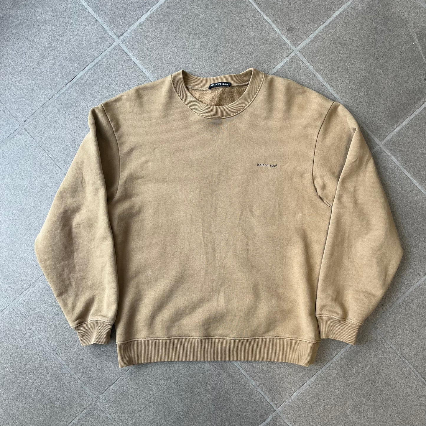 Balenciaga 2019 Khaki Small Logo Crewneck features a khaki 100% cotton construction with thick ribbed hems. A small black Balenciaga copyright logo is printed on the left chest. Made in Portugal.