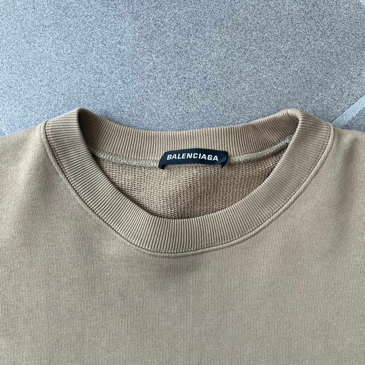 Balenciaga 2019 Khaki Small Logo Crewneck features a khaki 100% cotton construction with thick ribbed hems. A small black Balenciaga copyright logo is printed on the left chest. Made in Portugal.