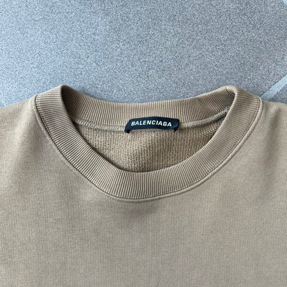 Balenciaga 2019 Khaki Small Logo Crewneck features a khaki 100% cotton construction with thick ribbed hems. A small black Balenciaga copyright logo is printed on the left chest. Made in Portugal.