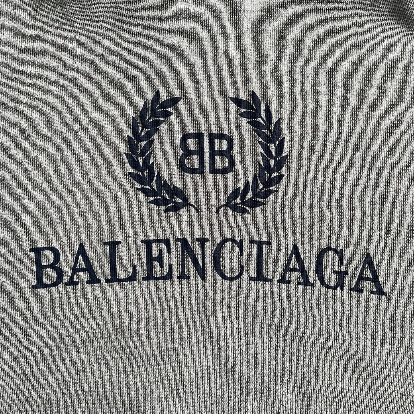 Balenciaga BB Crest Logo Hoodie in Heather Grey, crafted in Portugal from a heavyweight cotton-blend fleece (76% cotton, 24% polyester). The heather grey base features a dark navy BB emblem framed by laurel leaves and the Balenciaga logo text. Finished with dropped shoulders, ribbed edges, and a spacious front pocket, this oversized hoodie exemplifies elevated comfort and craftsmanship.