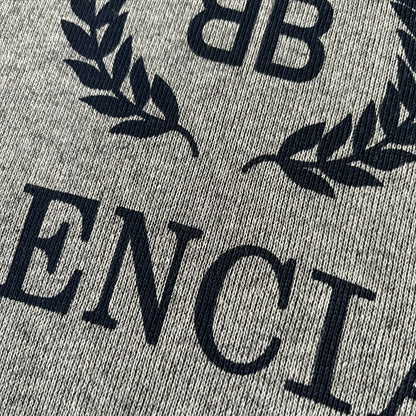 Balenciaga BB Crest Logo Hoodie in Heather Grey, crafted in Portugal from a heavyweight cotton-blend fleece (76% cotton, 24% polyester). The heather grey base features a dark navy BB emblem framed by laurel leaves and the Balenciaga logo text. Finished with dropped shoulders, ribbed edges, and a spacious front pocket, this oversized hoodie exemplifies elevated comfort and craftsmanship.
