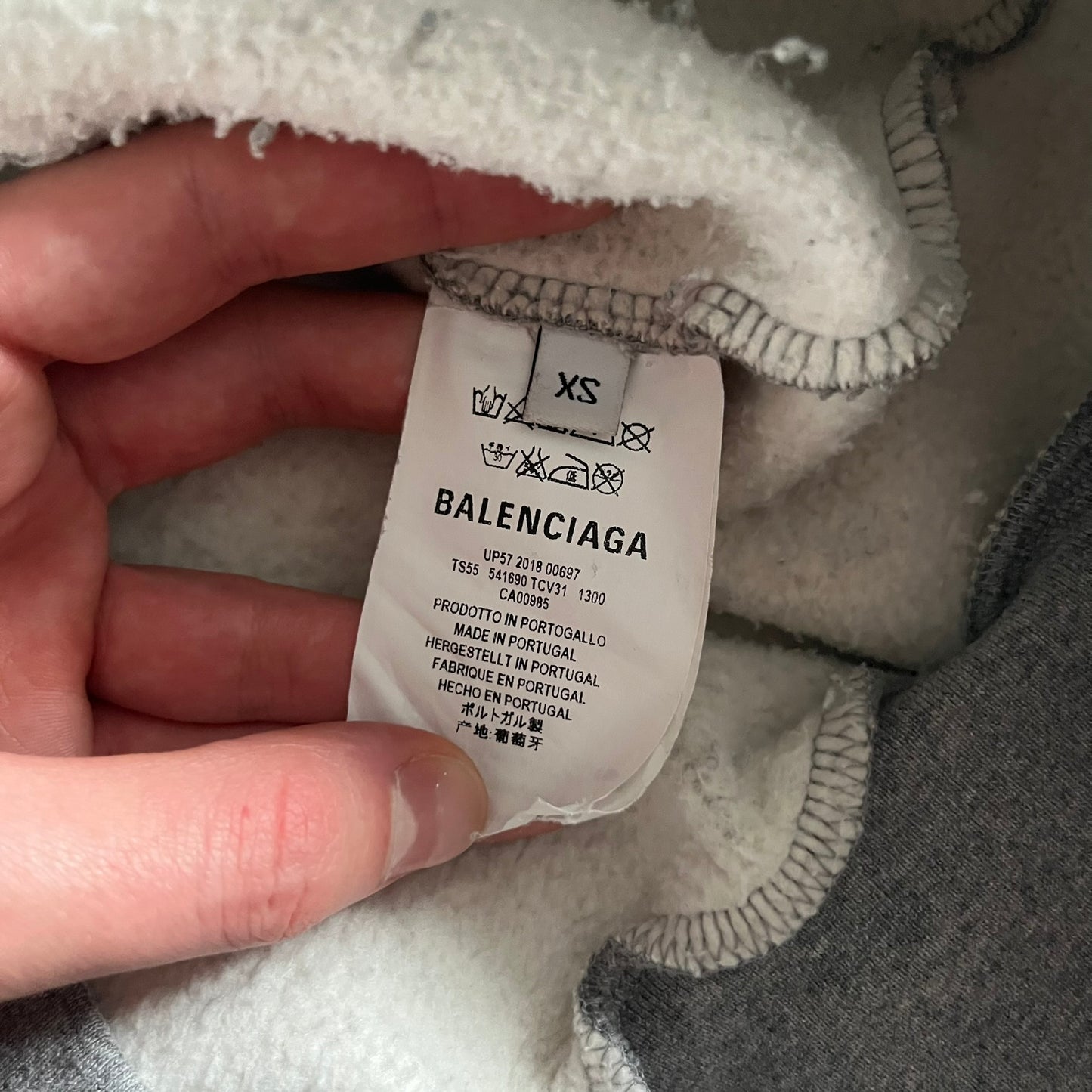 Balenciaga BB Crest Logo Hoodie in Heather Grey, crafted in Portugal from a heavyweight cotton-blend fleece (76% cotton, 24% polyester). The heather grey base features a dark navy BB emblem framed by laurel leaves and the Balenciaga logo text. Finished with dropped shoulders, ribbed edges, and a spacious front pocket, this oversized hoodie exemplifies elevated comfort and craftsmanship.