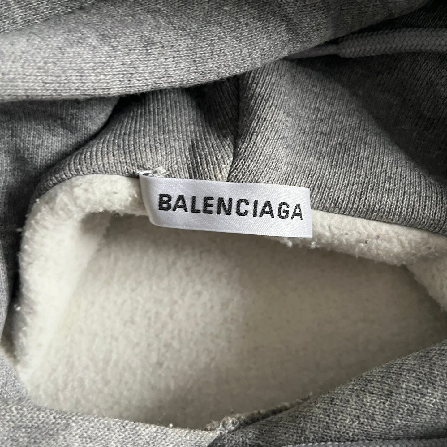 Balenciaga BB Crest Logo Hoodie in Heather Grey, crafted in Portugal from a heavyweight cotton-blend fleece (76% cotton, 24% polyester). The heather grey base features a dark navy BB emblem framed by laurel leaves and the Balenciaga logo text. Finished with dropped shoulders, ribbed edges, and a spacious front pocket, this oversized hoodie exemplifies elevated comfort and craftsmanship.