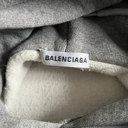 Balenciaga BB Crest Logo Hoodie in Heather Grey, crafted in Portugal from a heavyweight cotton-blend fleece (76% cotton, 24% polyester). The heather grey base features a dark navy BB emblem framed by laurel leaves and the Balenciaga logo text. Finished with dropped shoulders, ribbed edges, and a spacious front pocket, this oversized hoodie exemplifies elevated comfort and craftsmanship.