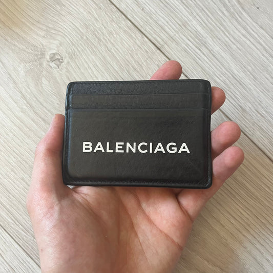  Balenciaga black leather card holder crafted in Italy from grained calfskin, featuring the updated Balenciaga logo in white inspired by public signage. Designed with four card slots and a central compartment, all fully lined in leather for durability. A sleek and practical accessory, it comes with a presentation box, reflecting Balenciaga’s modern luxury aesthetic under Demna Gvasalia’s creative direction.