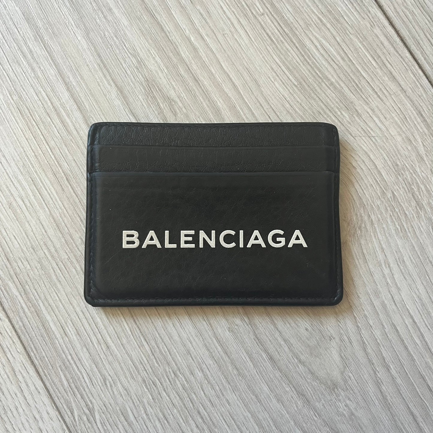  Balenciaga black leather card holder crafted in Italy from grained calfskin, featuring the updated Balenciaga logo in white inspired by public signage. Designed with four card slots and a central compartment, all fully lined in leather for durability. A sleek and practical accessory, it comes with a presentation box, reflecting Balenciaga’s modern luxury aesthetic under Demna Gvasalia’s creative direction.