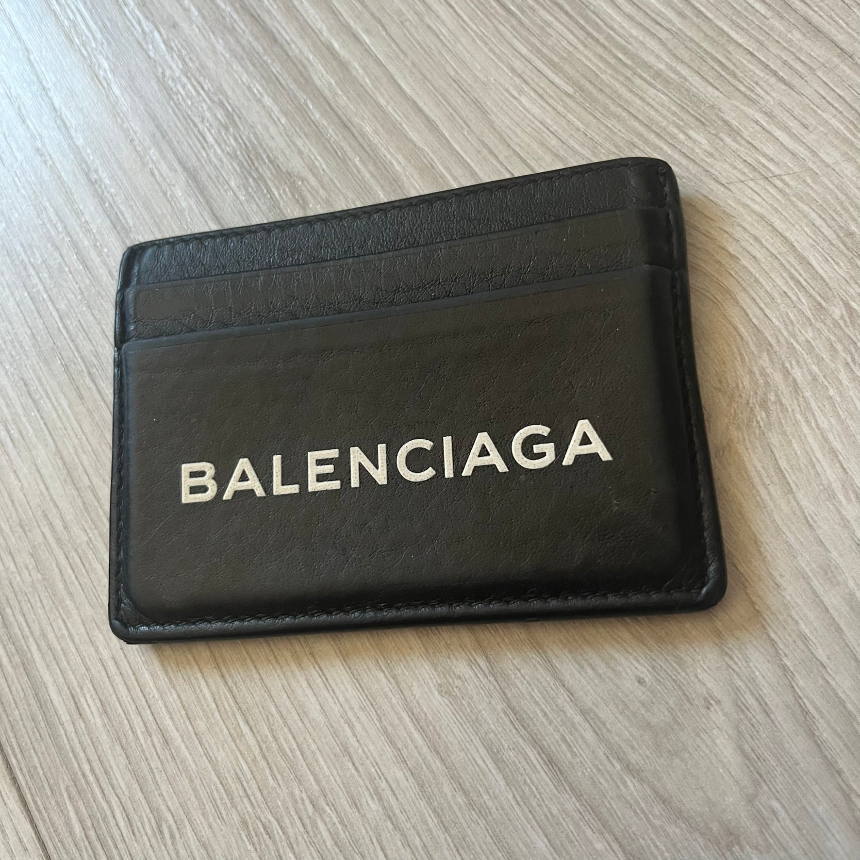  Balenciaga black leather card holder crafted in Italy from grained calfskin, featuring the updated Balenciaga logo in white inspired by public signage. Designed with four card slots and a central compartment, all fully lined in leather for durability. A sleek and practical accessory, it comes with a presentation box, reflecting Balenciaga’s modern luxury aesthetic under Demna Gvasalia’s creative direction.