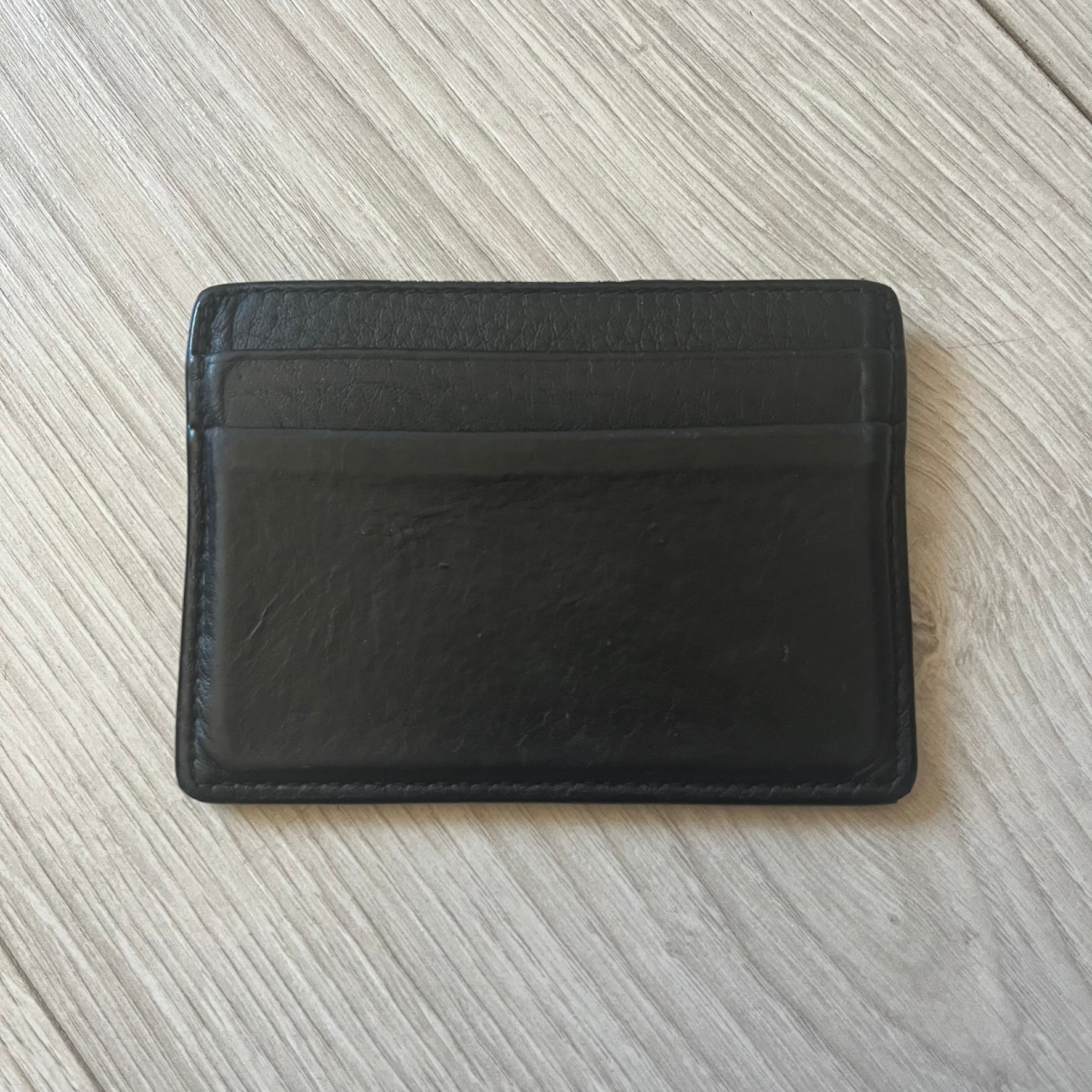  Balenciaga black leather card holder crafted in Italy from grained calfskin, featuring the updated Balenciaga logo in white inspired by public signage. Designed with four card slots and a central compartment, all fully lined in leather for durability. A sleek and practical accessory, it comes with a presentation box, reflecting Balenciaga’s modern luxury aesthetic under Demna Gvasalia’s creative direction.