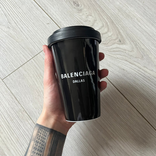 Balenciaga Dallas Black Coffee Cup crafted from glossy black porcelain with a white interior. Features a bold white Balenciaga logo with “Dallas” text underneath and a matching black rubber lid. A refined collectible showcasing everyday luxury.&nbsp;
