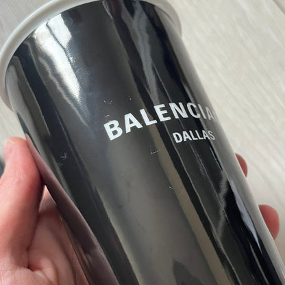 Balenciaga Dallas Black Coffee Cup crafted from glossy black porcelain with a white interior. Features a bold white Balenciaga logo with “Dallas” text underneath and a matching black rubber lid. A refined collectible showcasing everyday luxury.&nbsp;