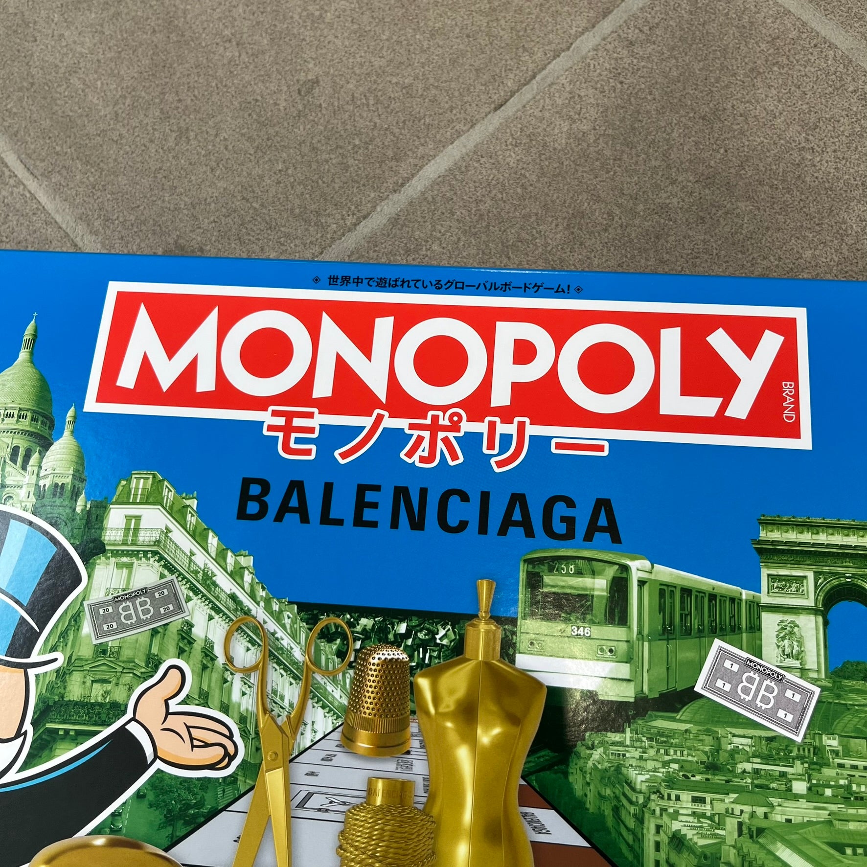 Balenciaga Monopoly 2025 VIP Gift Board Game features a custom Monopoly design made for Balenciaga. The game includes gold-tone fashion-themed playing pieces such as scissors, a thimble, thread spool, and mannequin. The board replaces standard properties with Balenciaga stores and locations, while the currency and cards feature Balenciaga branding and custom references including “Balenciaga Tax.”
