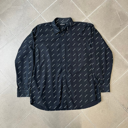 Balenciaga SS18 Black All-Over Logo Shirt is a black button-up made in Italy, featuring a diagonal all-over pattern of small white Balenciaga logo text and black buttons branded with Balenciaga. It has the archetype tag from the Spring/Summer 2018 collection.