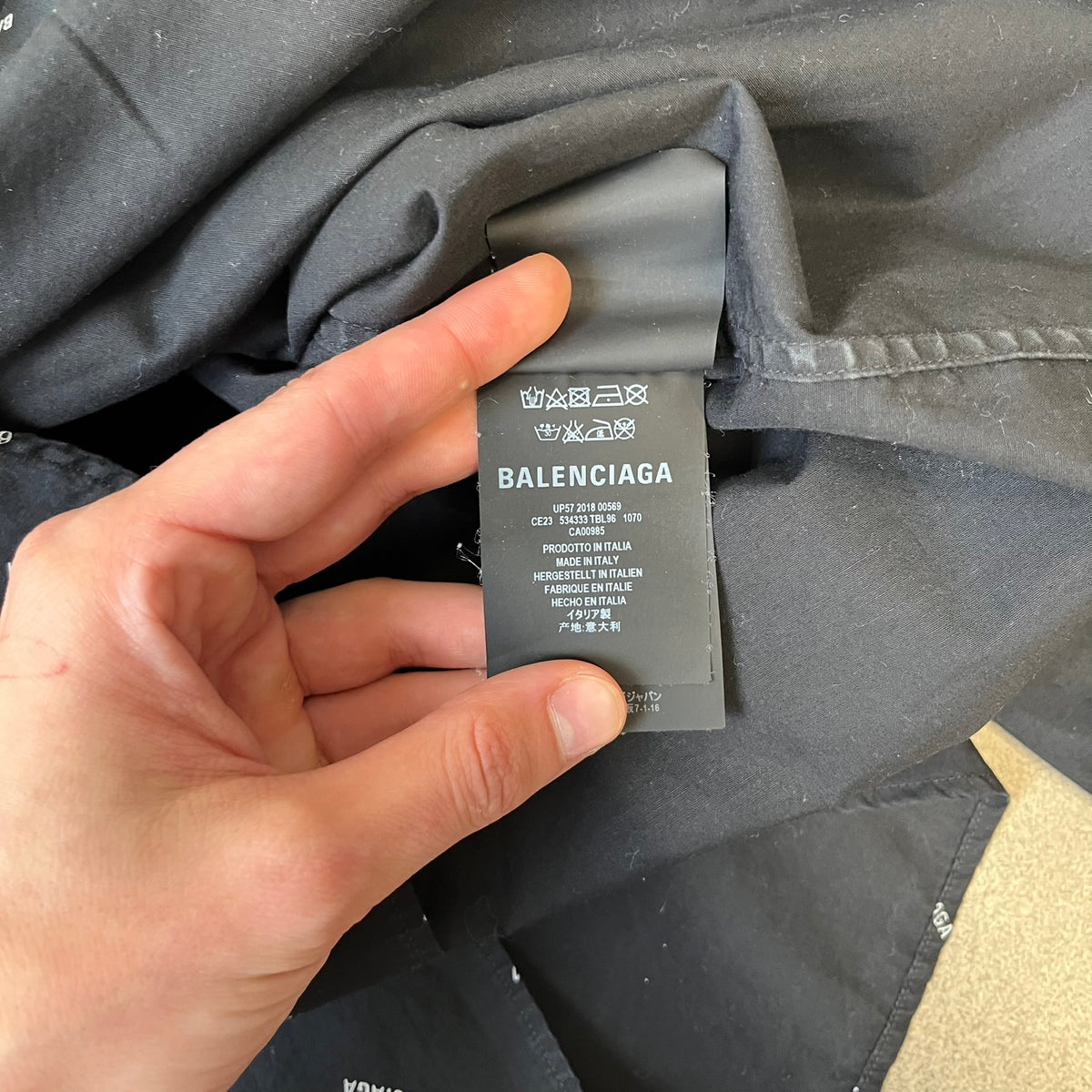 Balenciaga SS18 Black All-Over Logo Shirt is a black button-up made in Italy, featuring a diagonal all-over pattern of small white Balenciaga logo text and black buttons branded with Balenciaga. It has the archetype tag from the Spring/Summer 2018 collection.