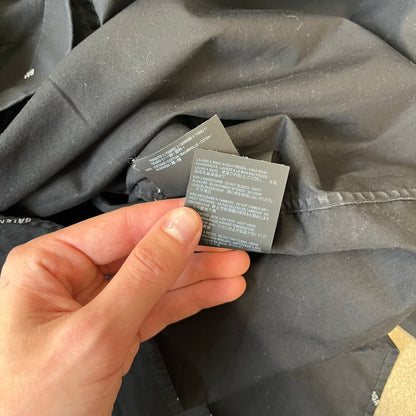 Balenciaga SS18 Black All-Over Logo Shirt is a black button-up made in Italy, featuring a diagonal all-over pattern of small white Balenciaga logo text and black buttons branded with Balenciaga. It has the archetype tag from the Spring/Summer 2018 collection.
