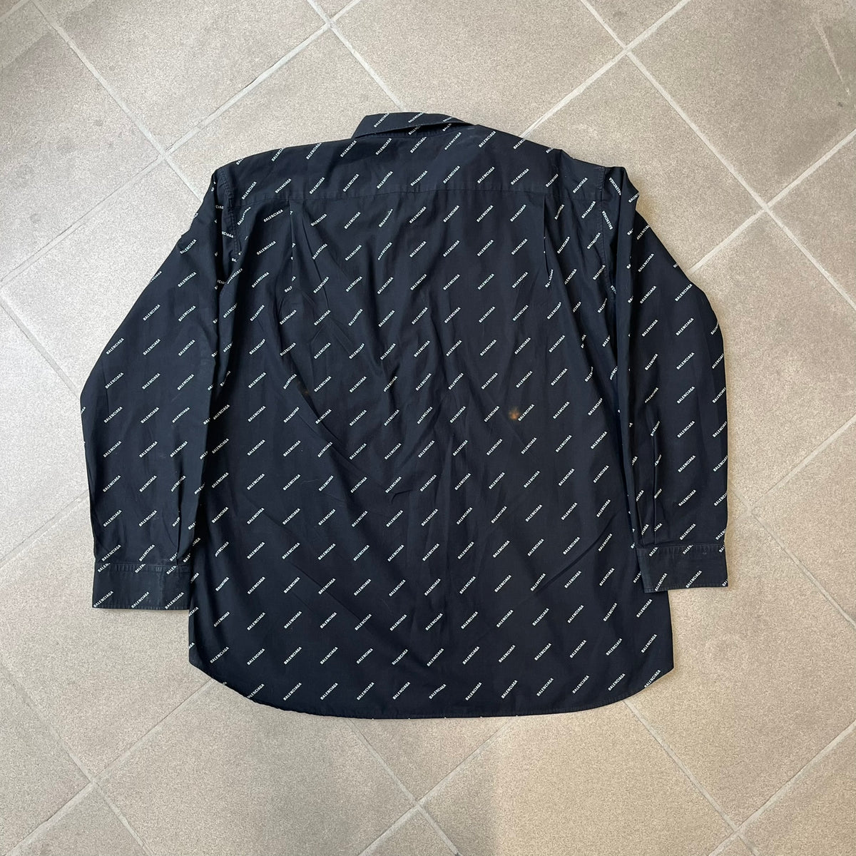 Balenciaga SS18 Black All-Over Logo Shirt is a black button-up made in Italy, featuring a diagonal all-over pattern of small white Balenciaga logo text and black buttons branded with Balenciaga. It has the archetype tag from the Spring/Summer 2018 collection.