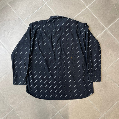 Balenciaga SS18 Black All-Over Logo Shirt is a black button-up made in Italy, featuring a diagonal all-over pattern of small white Balenciaga logo text and black buttons branded with Balenciaga. It has the archetype tag from the Spring/Summer 2018 collection.