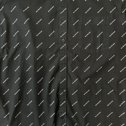 Balenciaga SS18 Black All-Over Logo Shirt is a black button-up made in Italy, featuring a diagonal all-over pattern of small white Balenciaga logo text and black buttons branded with Balenciaga. It has the archetype tag from the Spring/Summer 2018 collection.