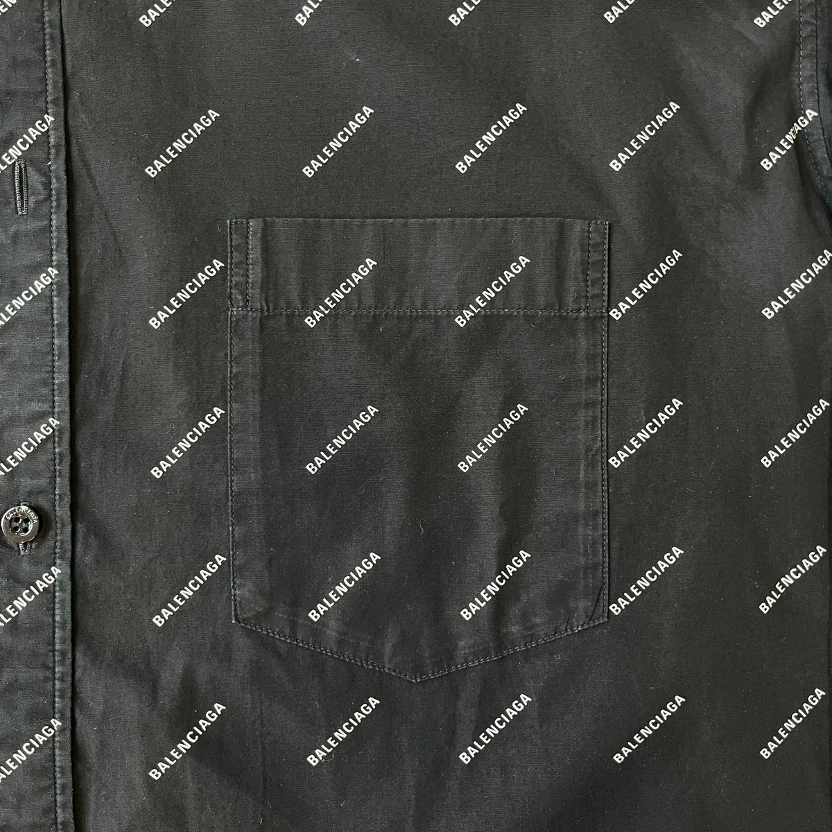 Balenciaga SS18 Black All-Over Logo Shirt is a black button-up made in Italy, featuring a diagonal all-over pattern of small white Balenciaga logo text and black buttons branded with Balenciaga. It has the archetype tag from the Spring/Summer 2018 collection.