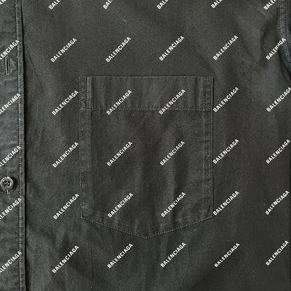 Balenciaga SS18 Black All-Over Logo Shirt is a black button-up made in Italy, featuring a diagonal all-over pattern of small white Balenciaga logo text and black buttons branded with Balenciaga. It has the archetype tag from the Spring/Summer 2018 collection.