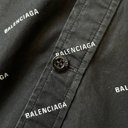 Balenciaga SS18 Black All-Over Logo Shirt is a black button-up made in Italy, featuring a diagonal all-over pattern of small white Balenciaga logo text and black buttons branded with Balenciaga. It has the archetype tag from the Spring/Summer 2018 collection.
