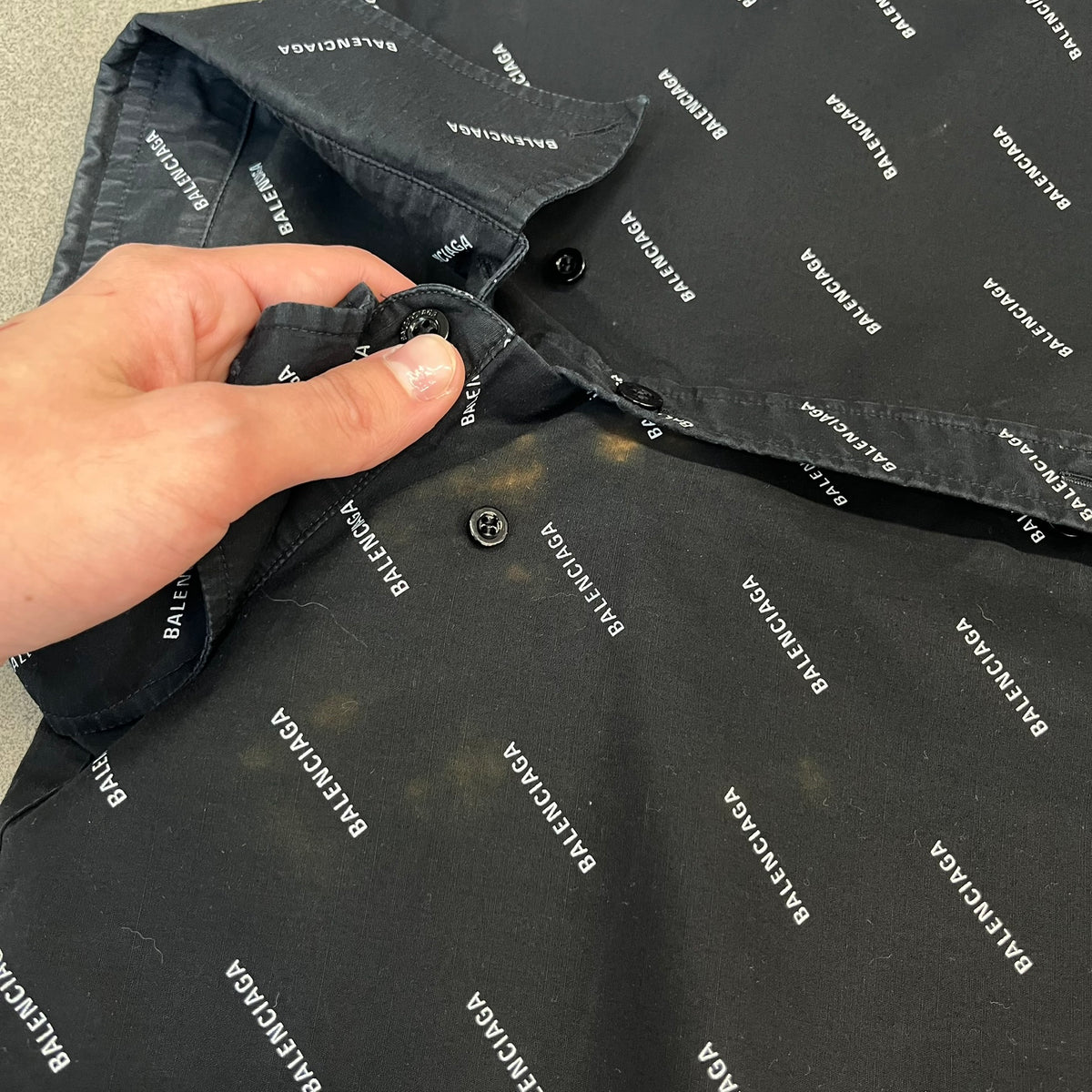 Balenciaga SS18 Black All-Over Logo Shirt is a black button-up made in Italy, featuring a diagonal all-over pattern of small white Balenciaga logo text and black buttons branded with Balenciaga. It has the archetype tag from the Spring/Summer 2018 collection.