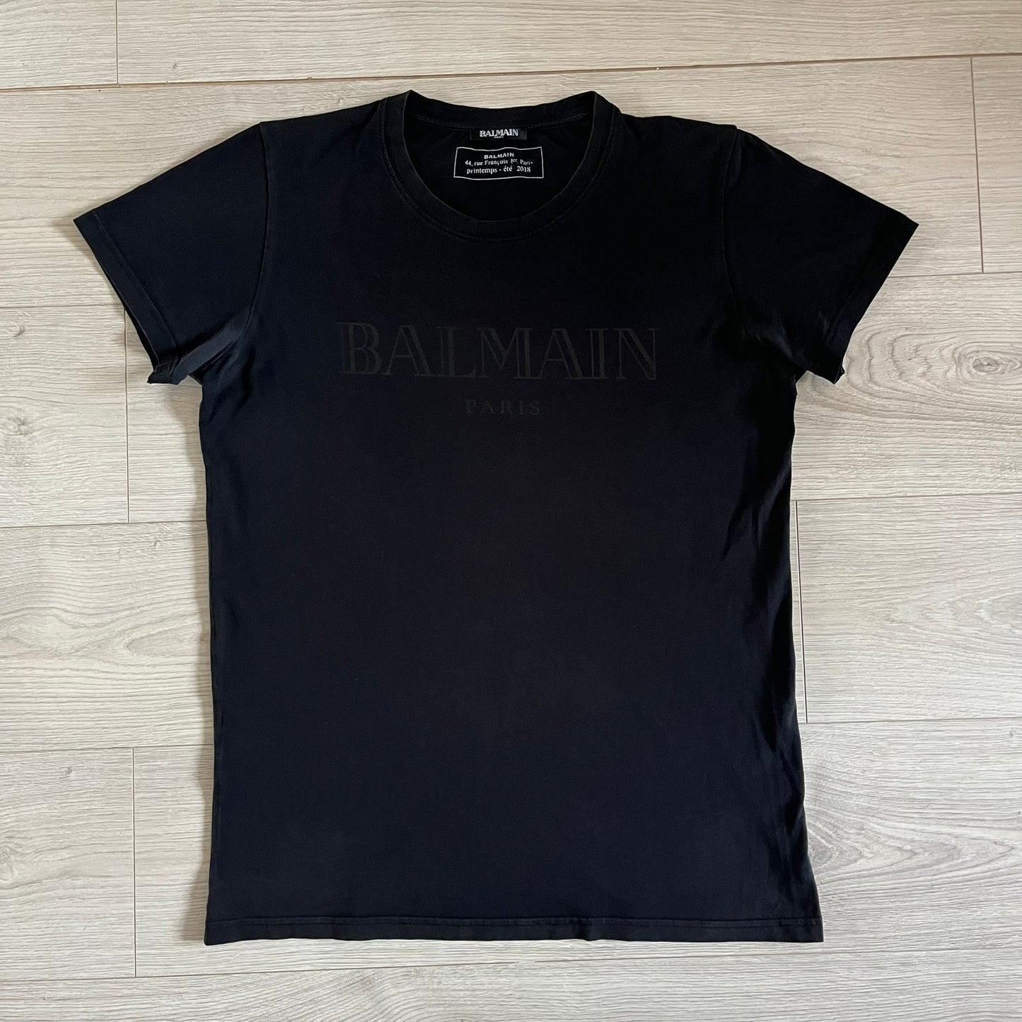 Balmain 2018 Black Tee featuring a discreet black Balmain Paris logo across the chest for a low-key, monochromatic effect. Constructed from soft 100% cotton and produced in Portugal, it embodies the brand’s modern, minimal direction.