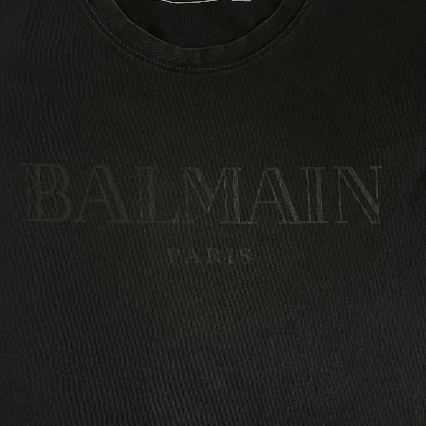Balmain 2018 Black Tee featuring a discreet black Balmain Paris logo across the chest for a low-key, monochromatic effect. Constructed from soft 100% cotton and produced in Portugal, it embodies the brand’s modern, minimal direction.