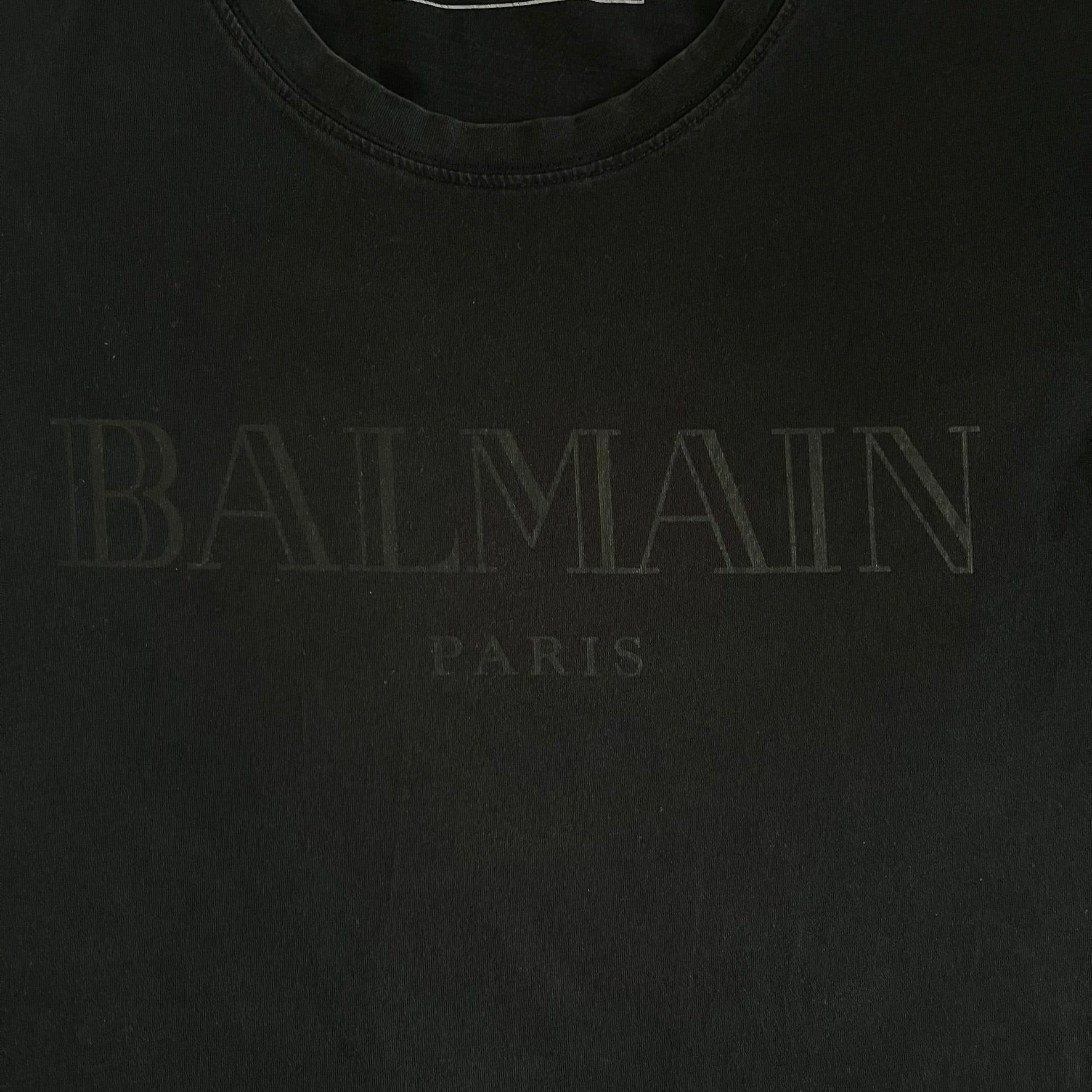Balmain 2018 Black Tee featuring a discreet black Balmain Paris logo across the chest for a low-key, monochromatic effect. Constructed from soft 100% cotton and produced in Portugal, it embodies the brand’s modern, minimal direction.