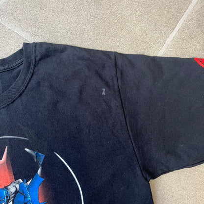 Batman 2005 Graphitti Red Logo Tee is a black T-shirt featuring a graphic of Batman in a blue suit running forward, set against a circular red Bat logo in the background. A red Graphitti logo is placed on one sleeve.