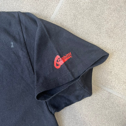 Batman 2005 Graphitti Red Logo Tee is a black T-shirt featuring a graphic of Batman in a blue suit running forward, set against a circular red Bat logo in the background. A red Graphitti logo is placed on one sleeve.