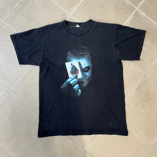 Batman The Dark Knight 2008 Joker Promo Tee features a black construction made on an Anvil blank, with Heath Ledger as the Joker holding a Batman playing card printed on the front. The upper back has The Dark Knight logo with small DC Comics 2008 licensing text underneath.
