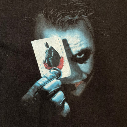 Batman The Dark Knight 2008 Joker Promo Tee features a black construction made on an Anvil blank, with Heath Ledger as the Joker holding a Batman playing card printed on the front. The upper back has The Dark Knight logo with small DC Comics 2008 licensing text underneath.
