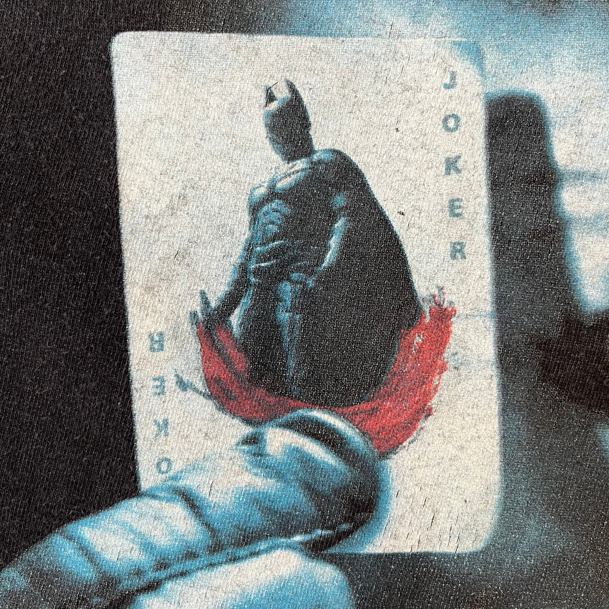 Batman The Dark Knight 2008 Joker Promo Tee features a black construction made on an Anvil blank, with Heath Ledger as the Joker holding a Batman playing card printed on the front. The upper back has The Dark Knight logo with small DC Comics 2008 licensing text underneath.
