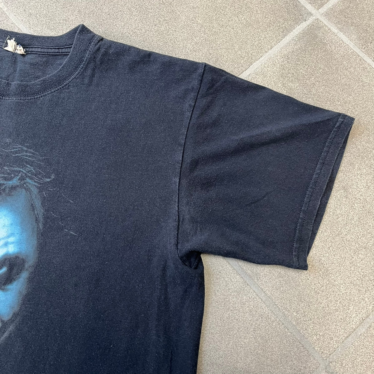 Batman The Dark Knight 2008 Joker Promo Tee features a black construction made on an Anvil blank, with Heath Ledger as the Joker holding a Batman playing card printed on the front. The upper back has The Dark Knight logo with small DC Comics 2008 licensing text underneath.
