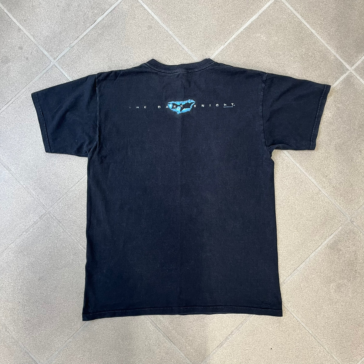 Batman The Dark Knight 2008 Joker Promo Tee features a black construction made on an Anvil blank, with Heath Ledger as the Joker holding a Batman playing card printed on the front. The upper back has The Dark Knight logo with small DC Comics 2008 licensing text underneath.
