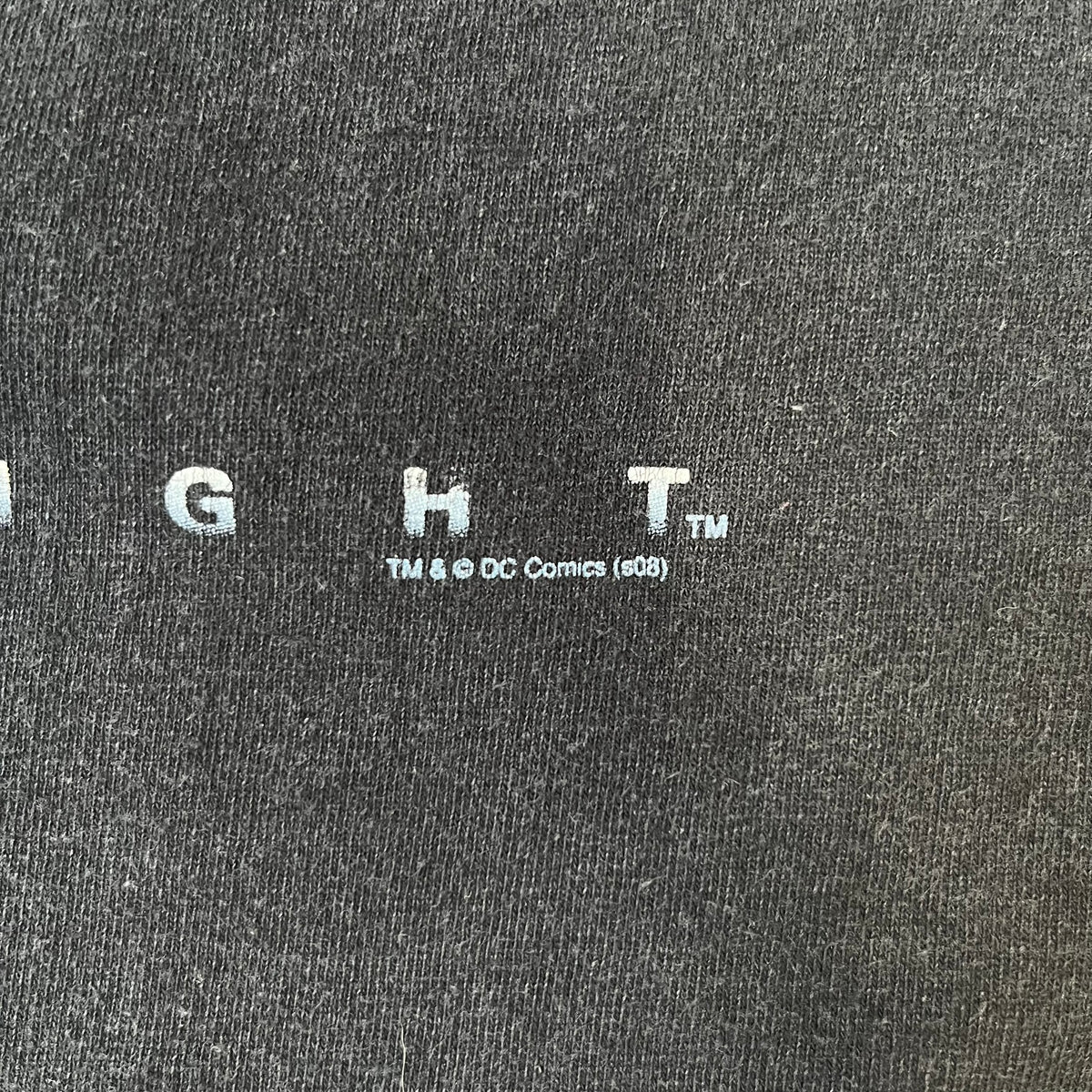 Batman The Dark Knight 2008 Joker Promo Tee features a black construction made on an Anvil blank, with Heath Ledger as the Joker holding a Batman playing card printed on the front. The upper back has The Dark Knight logo with small DC Comics 2008 licensing text underneath.
