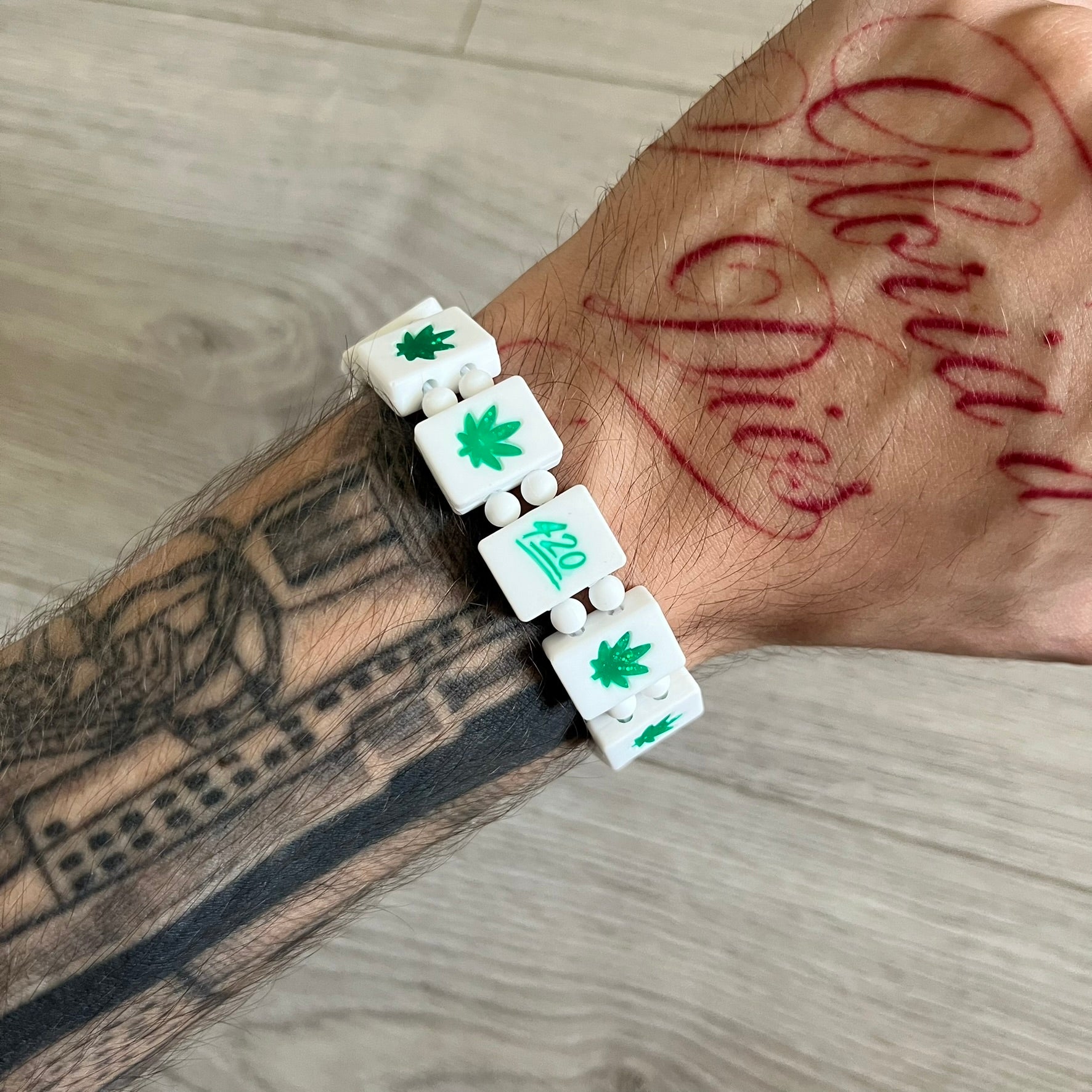 Bazo 1199 “420” Bracelet is a white silicone bead bracelet featuring glitter cannabis leaf graphics across the beads and a “420” emoji graphic on one bead. The interior includes a glitter red 1199 logo. It comes in the original plastic foil packaging.&nbsp;