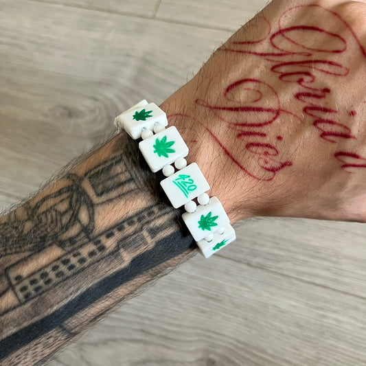 Bazo 1199 “420” Bracelet is a white silicone bead bracelet featuring glitter cannabis leaf graphics across the beads and a “420” emoji graphic on one bead. The interior includes a glitter red 1199 logo. It comes in the original plastic foil packaging.&nbsp;