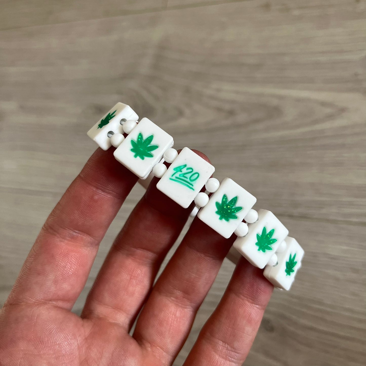 Bazo 1199 “420” Bracelet is a white silicone bead bracelet featuring glitter cannabis leaf graphics across the beads and a “420” emoji graphic on one bead. The interior includes a glitter red 1199 logo. It comes in the original plastic foil packaging.&nbsp;