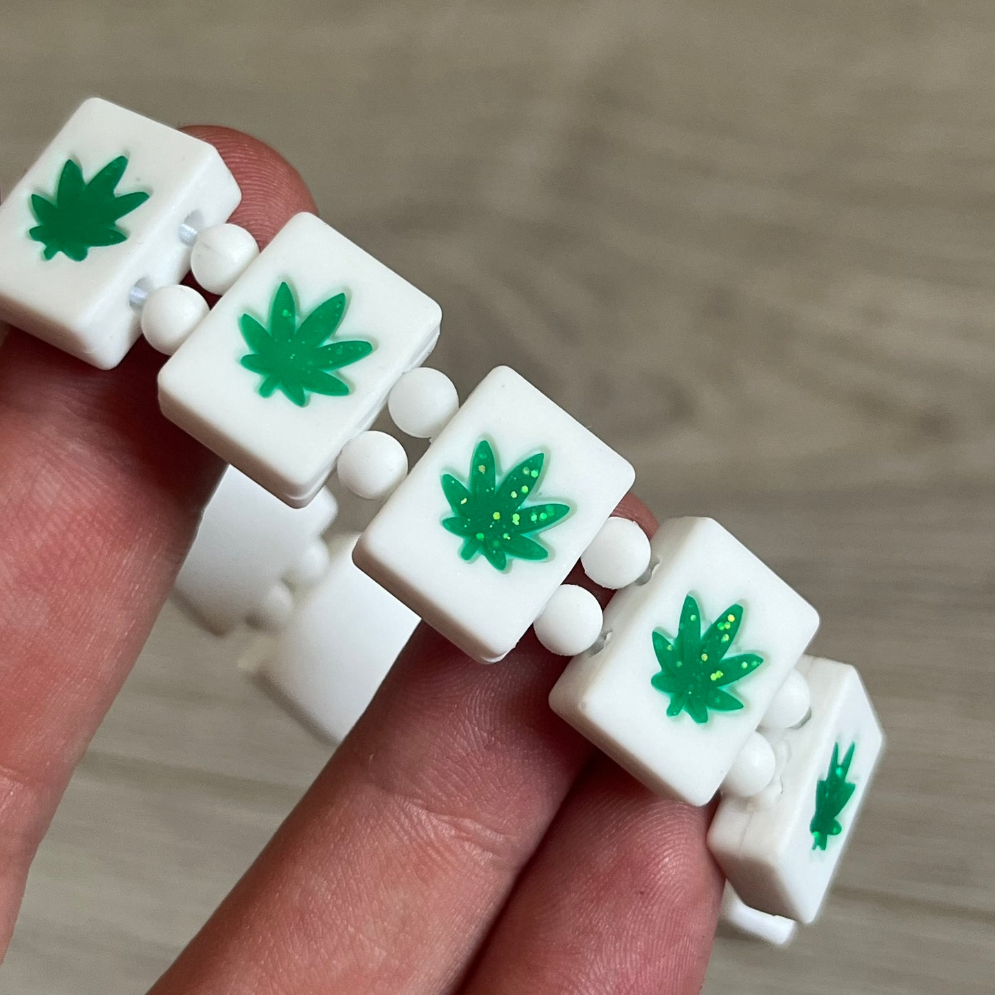 Bazo 1199 “420” Bracelet is a white silicone bead bracelet featuring glitter cannabis leaf graphics across the beads and a “420” emoji graphic on one bead. The interior includes a glitter red 1199 logo. It comes in the original plastic foil packaging.&nbsp;