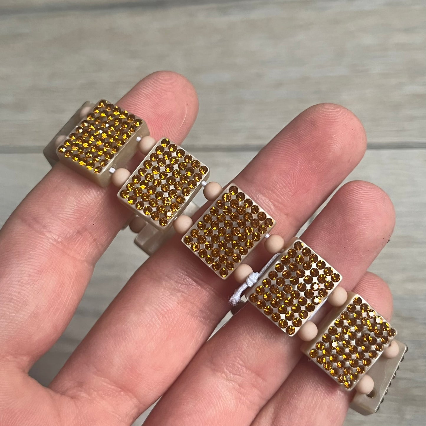 Bazo 1199 x 63KLUF Rhinestone Bracelet is a wooden bead bracelet from the 1199 and 63KLUF collaboration. The outer side is covered with gold and orange-toned rhinestones, while the inner side has a pearly beige finish. The interior is marked with black 1199 and 63KLUF logos.