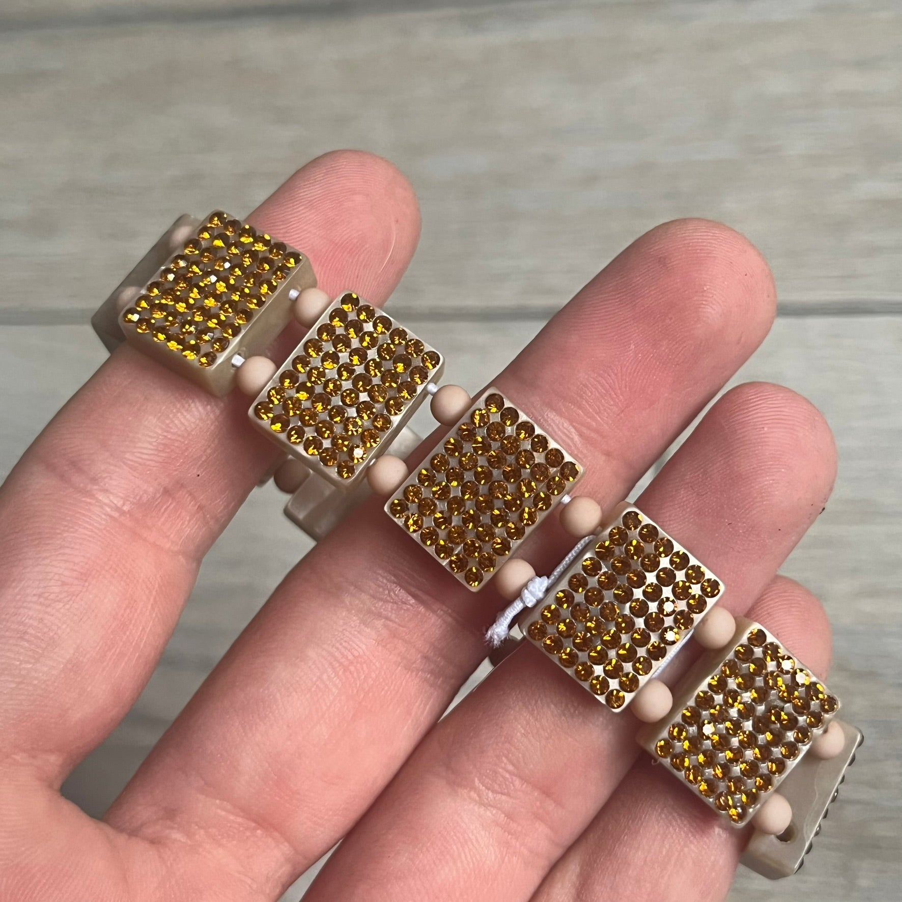 Bazo 1199 x 63KLUF Rhinestone Bracelet is a wooden bead bracelet from the 1199 and 63KLUF collaboration. The outer side is covered with gold and orange-toned rhinestones, while the inner side has a pearly beige finish. The interior is marked with black 1199 and 63KLUF logos.